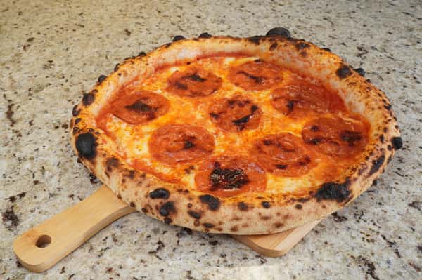 "Neapolitan-style pepperoni pizza with charred crust served on a wooden paddle over a granite countertop