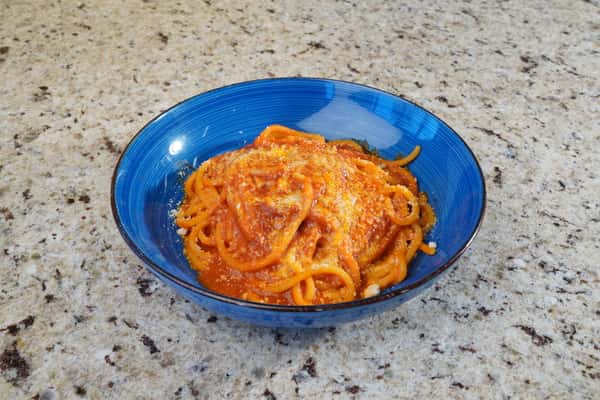 Spaghetti served with tomato sauce and grated cheese in a vibrant blue bowl on a granite countertop.