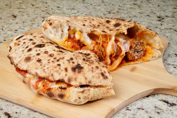 Meatball calzone with melted cheese and tomato sauce on a wooden board