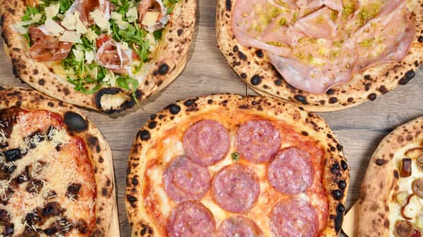 Assorted Neapolitan-style pizzas including salami, prosciutto with arugula, mortadella with pistachio, and grilled vegetables on a rustic wooden board