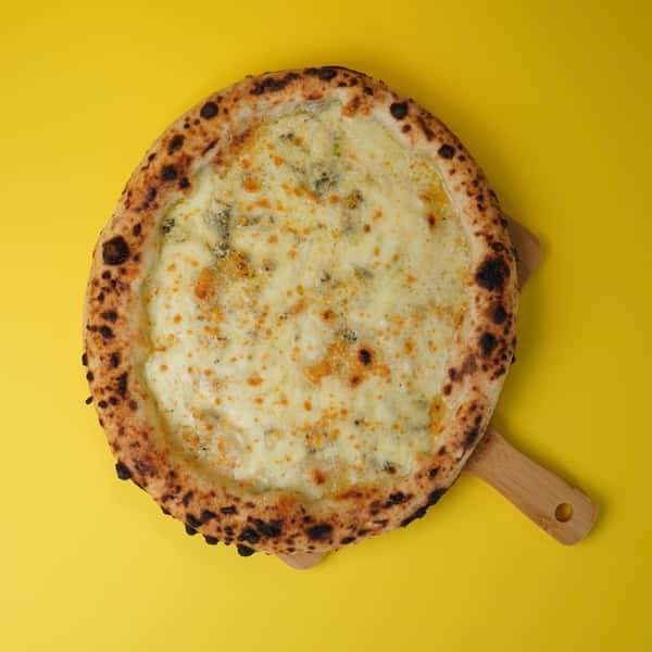 four cheese pizza on wooden peel over yellow background