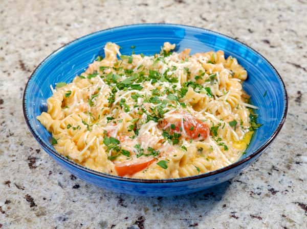 Creamy fusilli pasta with tomatoes and parsley in a blue bowl