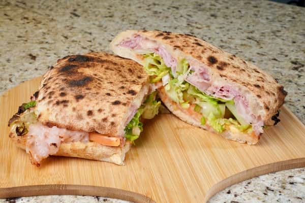 Toasted Italian sandwich with ham, lettuce, tomato, and cheese on wooden board