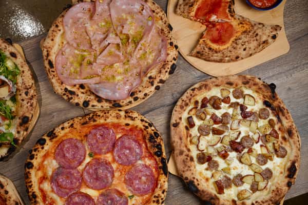 Assorted Neapolitan pizzas on wooden table including mortadella, potato, and salami varieties