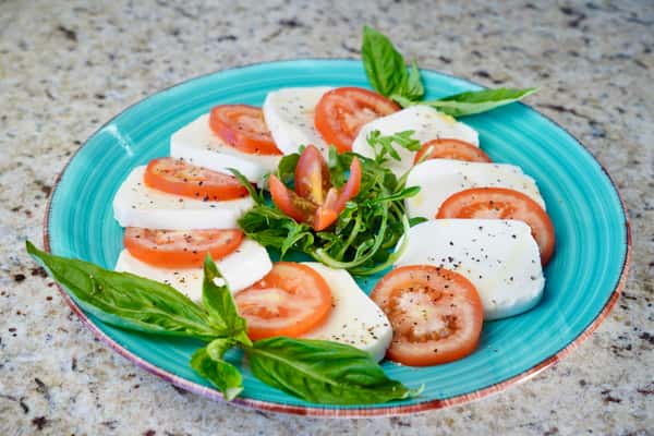 caprese salad with fresh mozzarella, tomato slices, basil, and arugula on a turquoise plate