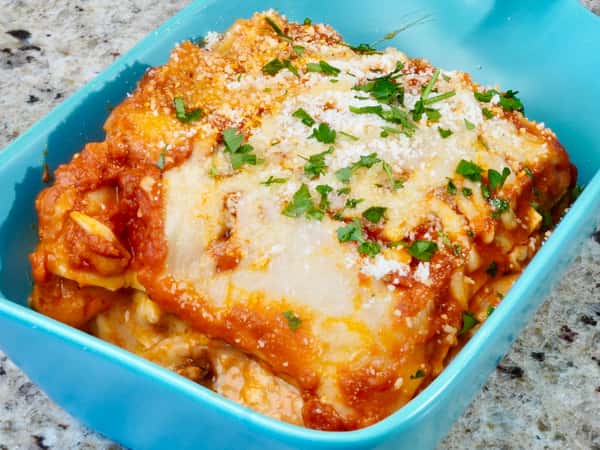 Baked lasagna with melted cheese and fresh parsley in a blue ceramic dish