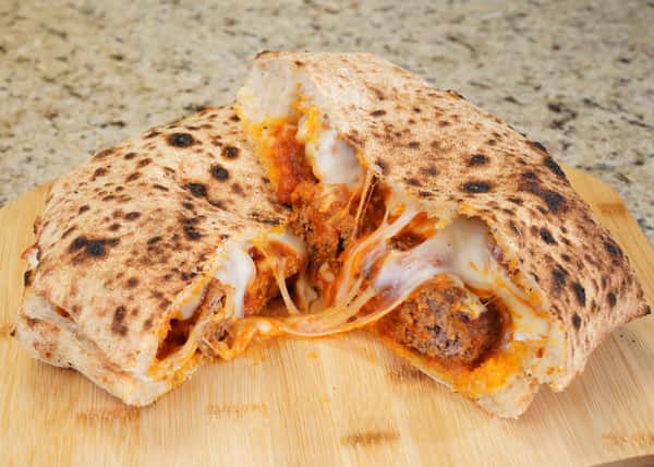 Stuffed calzone cut open, revealing meatballs, tomato sauce, and melted mozzarella cheese on a wooden board.