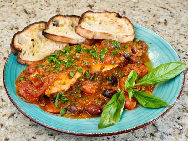 grilled chicken breast in puttanesca sauce with olives, cherry tomatoes, and toasted bread
