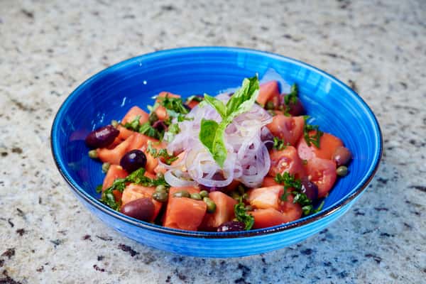Fresh tomato salad with red onions, black olives, capers, and basil.