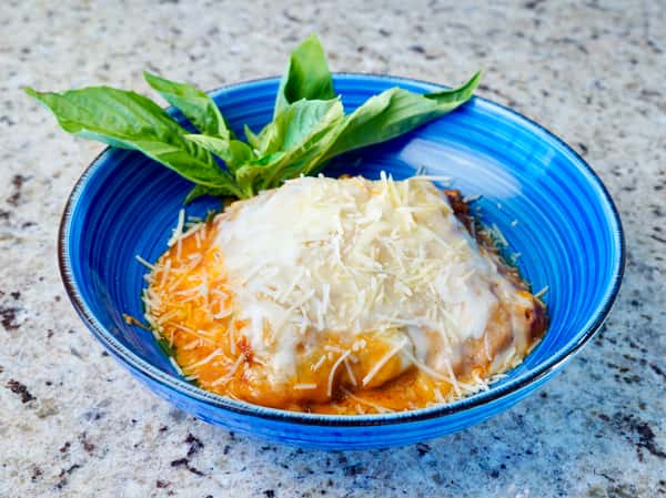 Stuffed pasta topped with melted cheese and tomato sauce, garnished with basil in a blue bowl