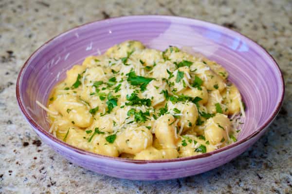 Creamy gnocchi with grated cheese and parsley in a purple bowl