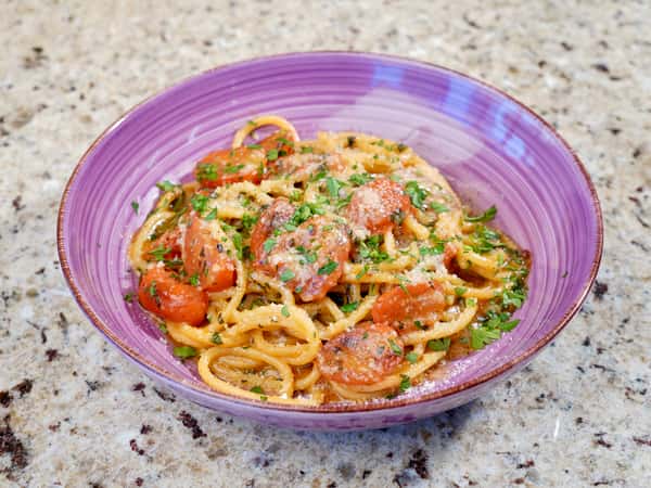 Spaghetti with cherry tomatoes and grated cheese in a purple bowl