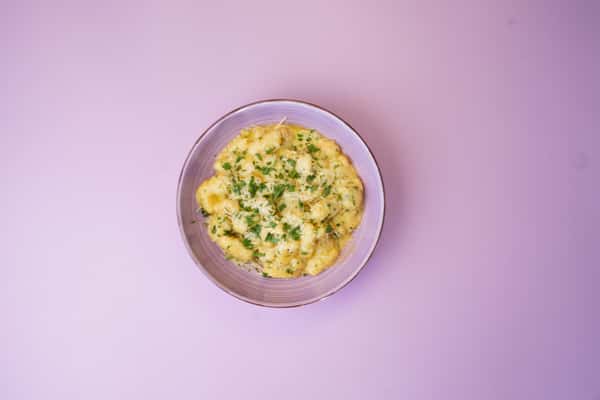 Creamy gnocchi garnished with chopped parsley in a white bowl on a pink background