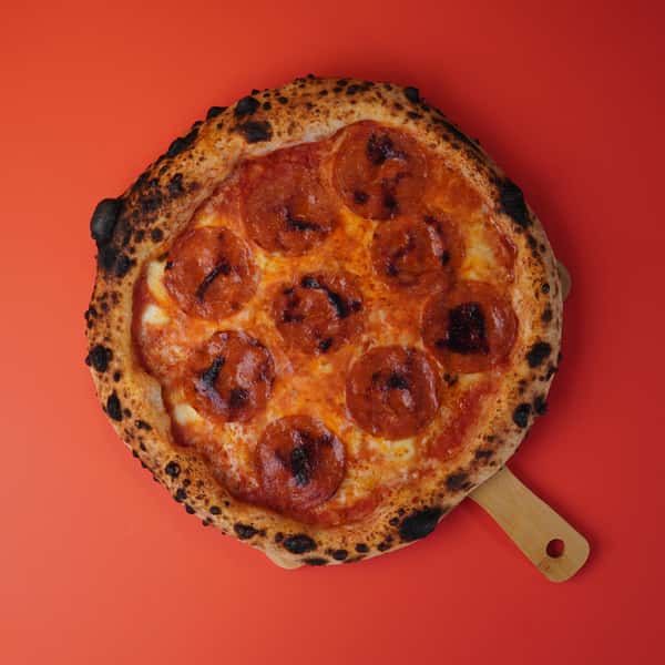 Neapolitan pepperoni pizza on wooden board over red background