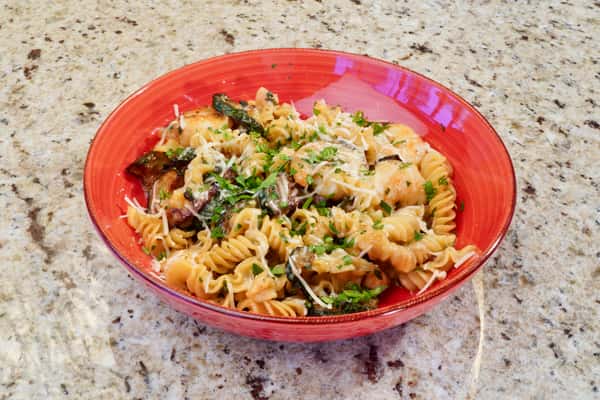 Rotini pasta with sautéed vegetables and grated cheese in a red bowl