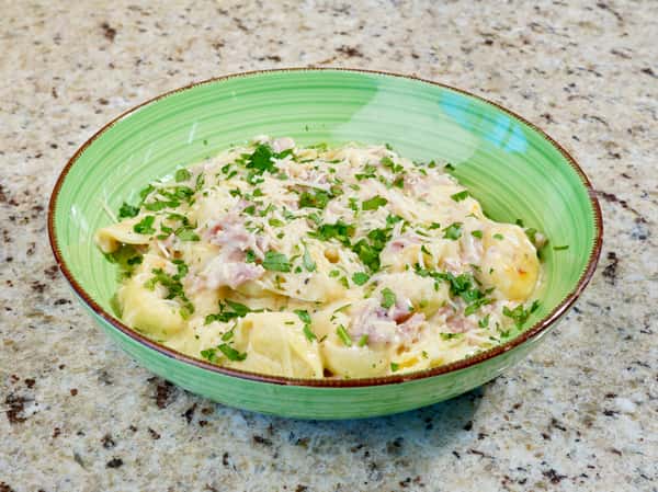 Creamy tortellini pasta with ham and parsley served in a green bowl