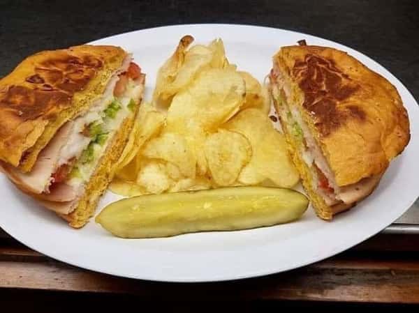 sandwich with deli meat, lettuce, tomato with chips and a pickle on the side