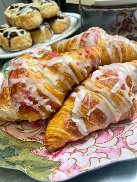Golden, flaky pastries drizzled with sweet icing are displayed fresh from the bakery, creating a warm and irresistible homemade treat presentation.