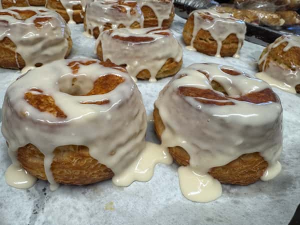 Fresh cinnamon rolls topped with creamy icing and crunchy nut pieces are displayed on a tray, creating a sweet and indulgent bakery presentation.