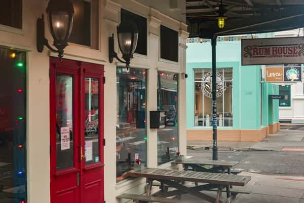 Street view of The Rum House Caribbean Taqueria with red doors, outdoor benches, and colorful holiday lights.