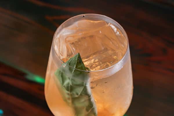 Sparkling cocktail served over large ice cubes in a stemless glass, garnished with a fresh basil leaf.