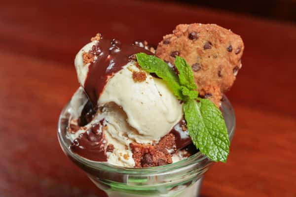 Vanilla ice cream topped with chocolate sauce, cookie crumbles, a chocolate chip cookie, and a fresh mint sprig.