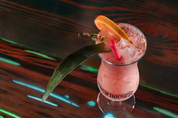 Pink frozen cocktail topped with ice, garnished with a pineapple slice and orange wedge, served with a red straw.