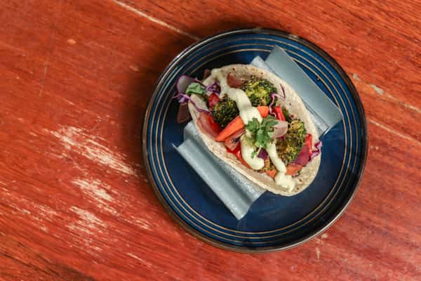 Grilled veggie taco filled with broccoli, carrots, onions, and cabbage, drizzled with creamy sauce and garnished with cilantro.