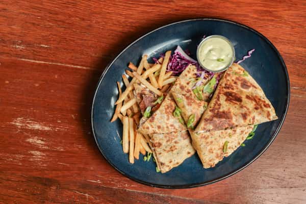 Grilled quesadilla slices filled with chicken and vegetables, served with golden French fries and garnished with green onions.