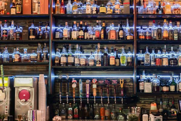 Bar shelves stocked with various liquor bottles and beer taps below, illuminated by blue LED lighting for a vibrant display.