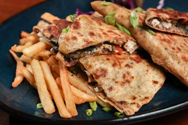 Grilled quesadilla slices filled with chicken and vegetables, served with golden French fries and garnished with green onions.