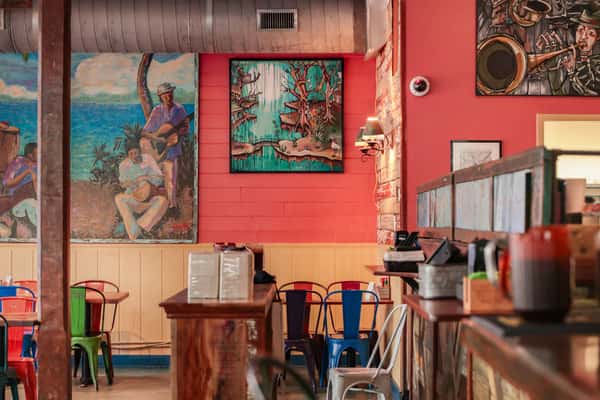 Colorful restaurant interior with red walls, vibrant murals, metal chairs, and a rustic counter, evoking a lively, artistic vibe.