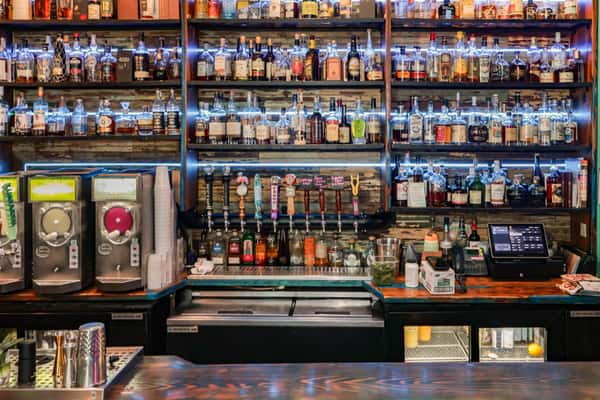Bar shelves stocked with various liquor bottles and beer taps below, illuminated by blue LED lighting for a vibrant display.
