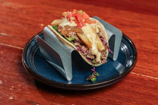 Soft taco filled with pulled pork, French fries, shredded greens, cheese sauce, and topped with fresh diced tomatoes.