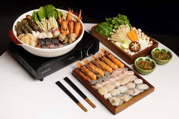 A Japanese set meal featuring a hot pot, sushi rolls, and side dishes with chopsticks