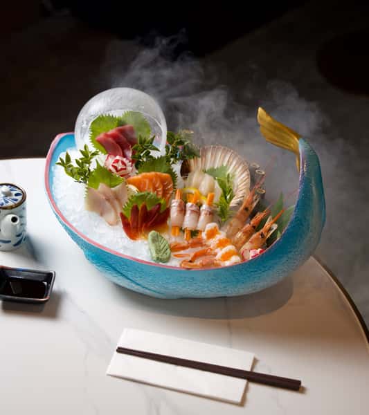 A bowl of fresh sushi and seafood garnished with vegetables, served with chopsticks