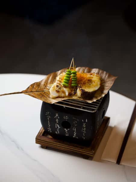 An elegantly plated Japanese dish in a black square container with garnish