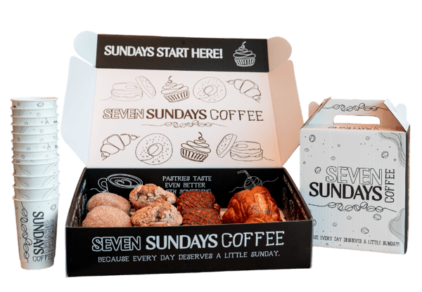 Box full of pastries beside a beverage carton and cups