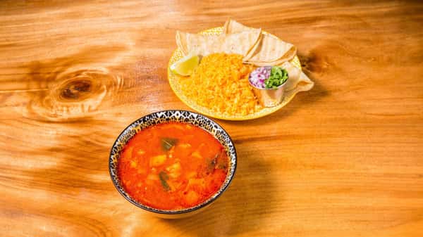 Bowl of homemade tortilla soup served with rice, chips, and salsa.