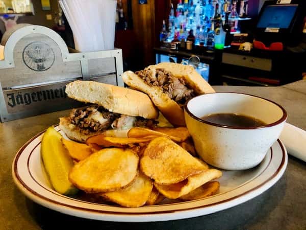 French Dip Sandwich: Sliced roast beef layered on a hoagie and topped with melted Swiss cheese. Served with hot au jus, chips and pickle spear
