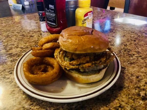 Queso Burger: 1/3 lb seasoned burger patty. Topped with jalapenos, queso cheese, lettuce, tomato, and crispy onion rings. Onion rings on the side.