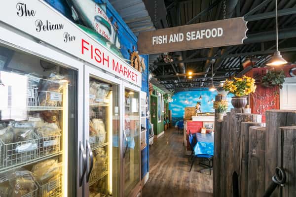 Indoor fish market section of a coastal-themed restaurant with glass-door freezers stocked with seafood and nautical décor.