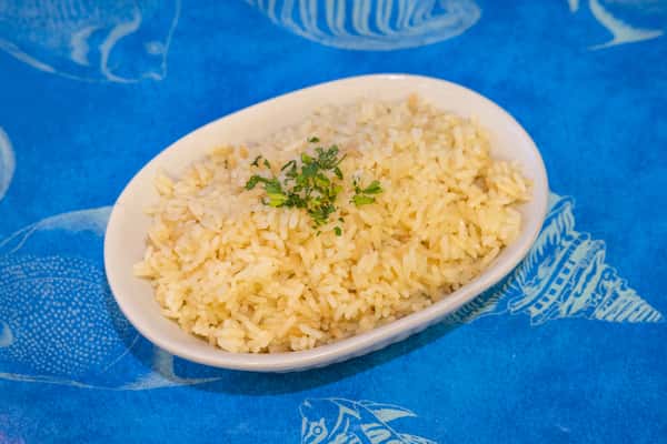 Fluffy seasoned white rice garnished with fresh parsley, served in a white oval bowl on a blue nautical-pattern tablecloth.