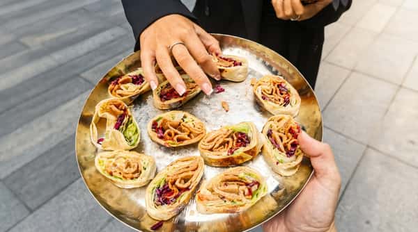 Flatbread wraps with meat and salad fillings on a metallic tray, being served.