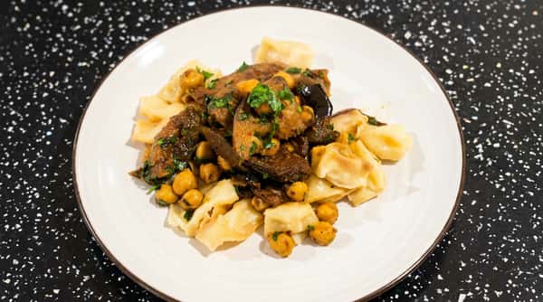 Stewed mushrooms and chickpeas with fresh parsley on a bed of wide, flat pasta on a white plate.