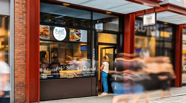 Storefront of Ebby's Turkish Kitchen with food menu displays and a woman standing in the doorway.