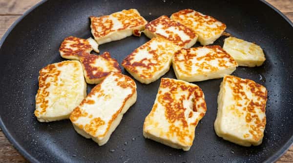 Slices of halloumi cheese frying in a dark pan, with golden-brown sear marks.