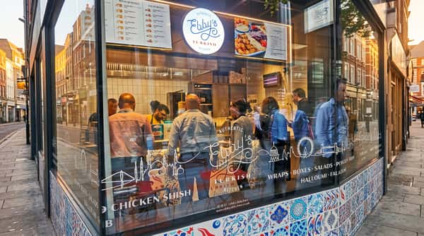 Exterior view of Ebby's Turkish Kitchen, showing customers and staff inside, reflected in a glass window with menu decals.