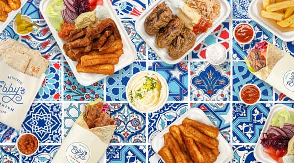 Various Turkish dishes on a white and blue patterned surface, including doner kebab, kofte, hummus, wraps, and fries.