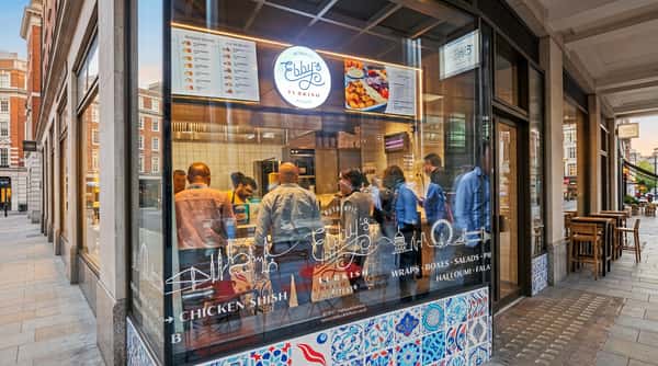 A restaurant storefront with a glowing "Ebby's Turkish Kitchen" sign, menus, and customers seen through the patterned glass.